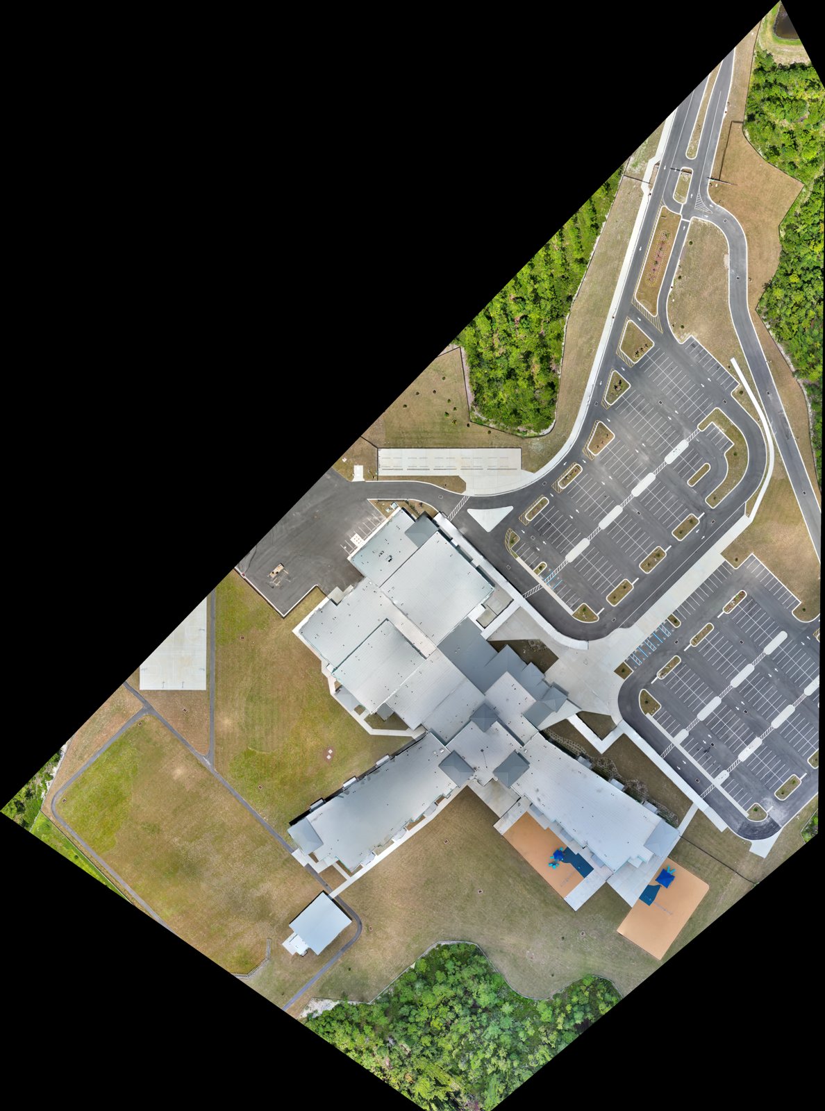 Georeferenced RGB orthomosaic of a single-story campus, roof planes, drive lanes and a full parking field resolved top-down.
