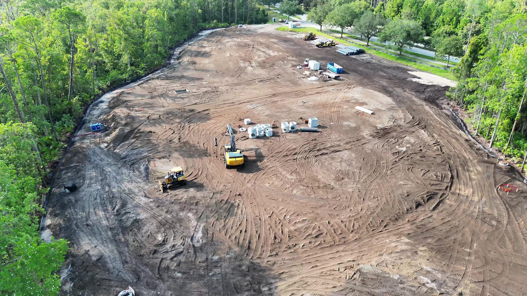Overhead aerial frame of the same earthwork site showing equipment, stockpiles, and haul-road tracking across the graded pad.